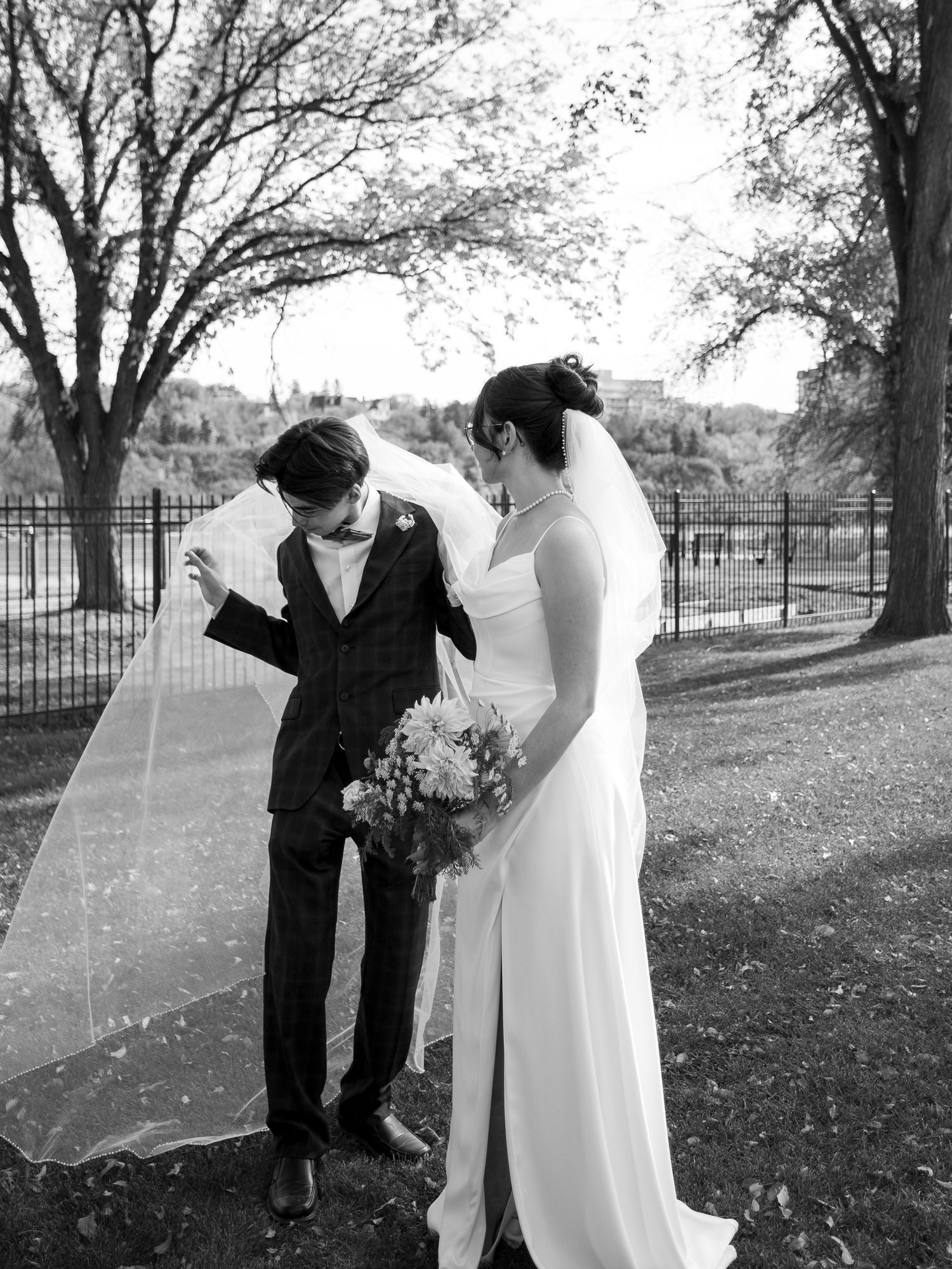 Playful wedding couple dancing together on an autumn lawn with trees in the background.