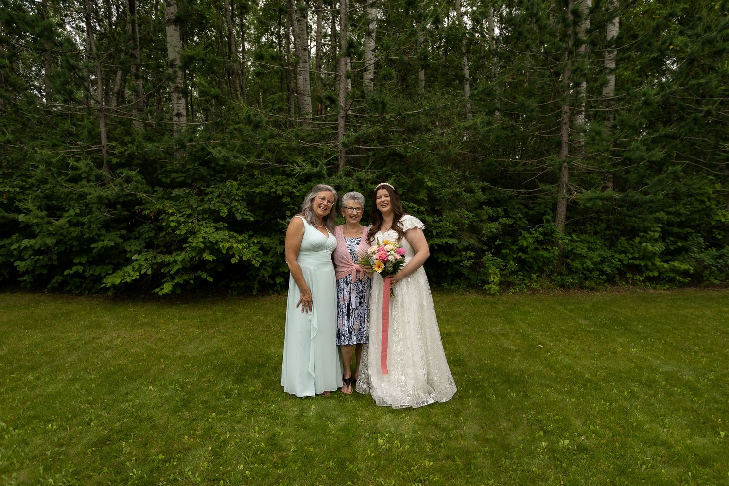 Wedding party poses for a photo in front of a wooded backdrop.