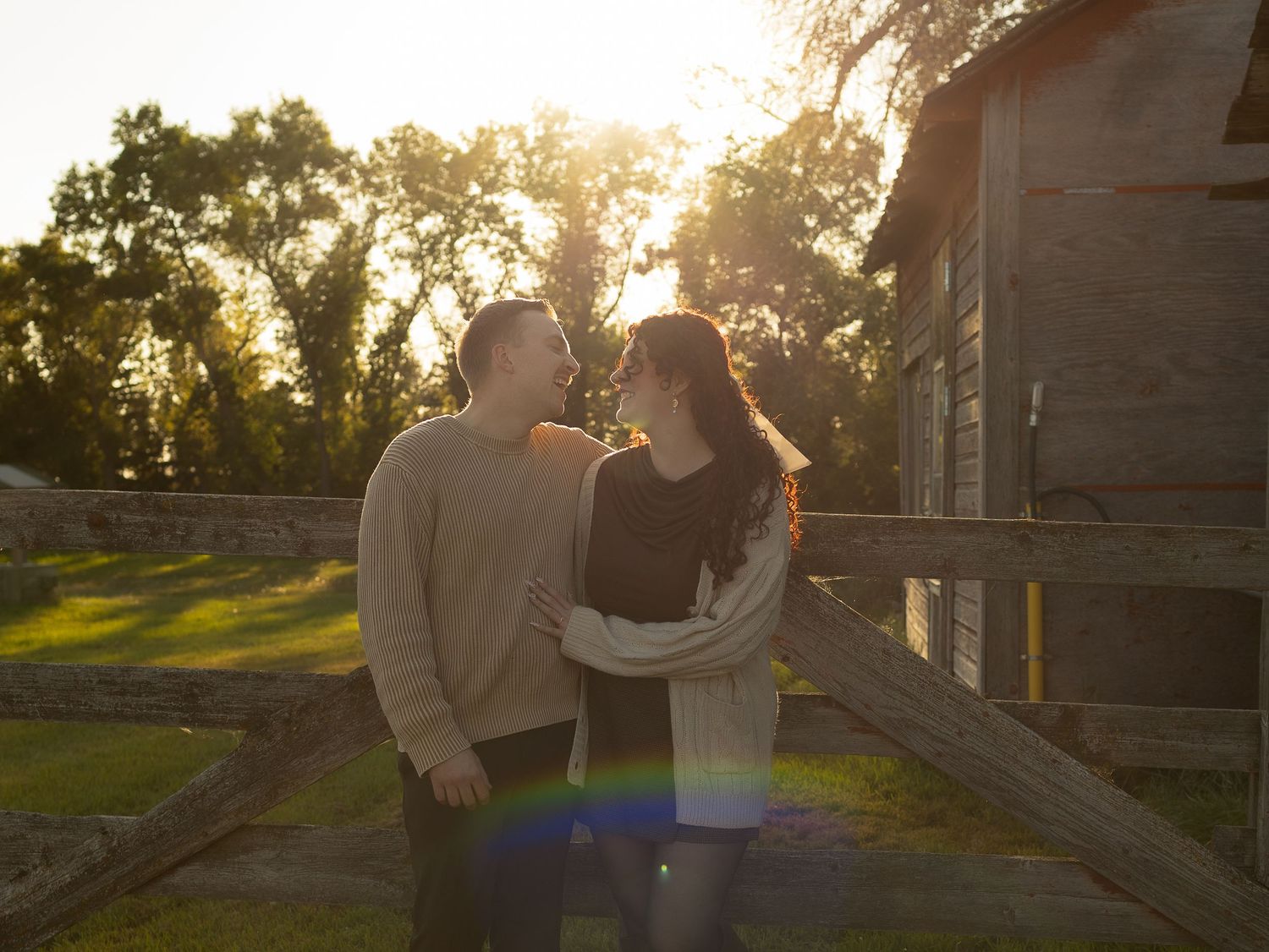 A couple sharing an intimate moment at sunset near a rustic wooden structure.