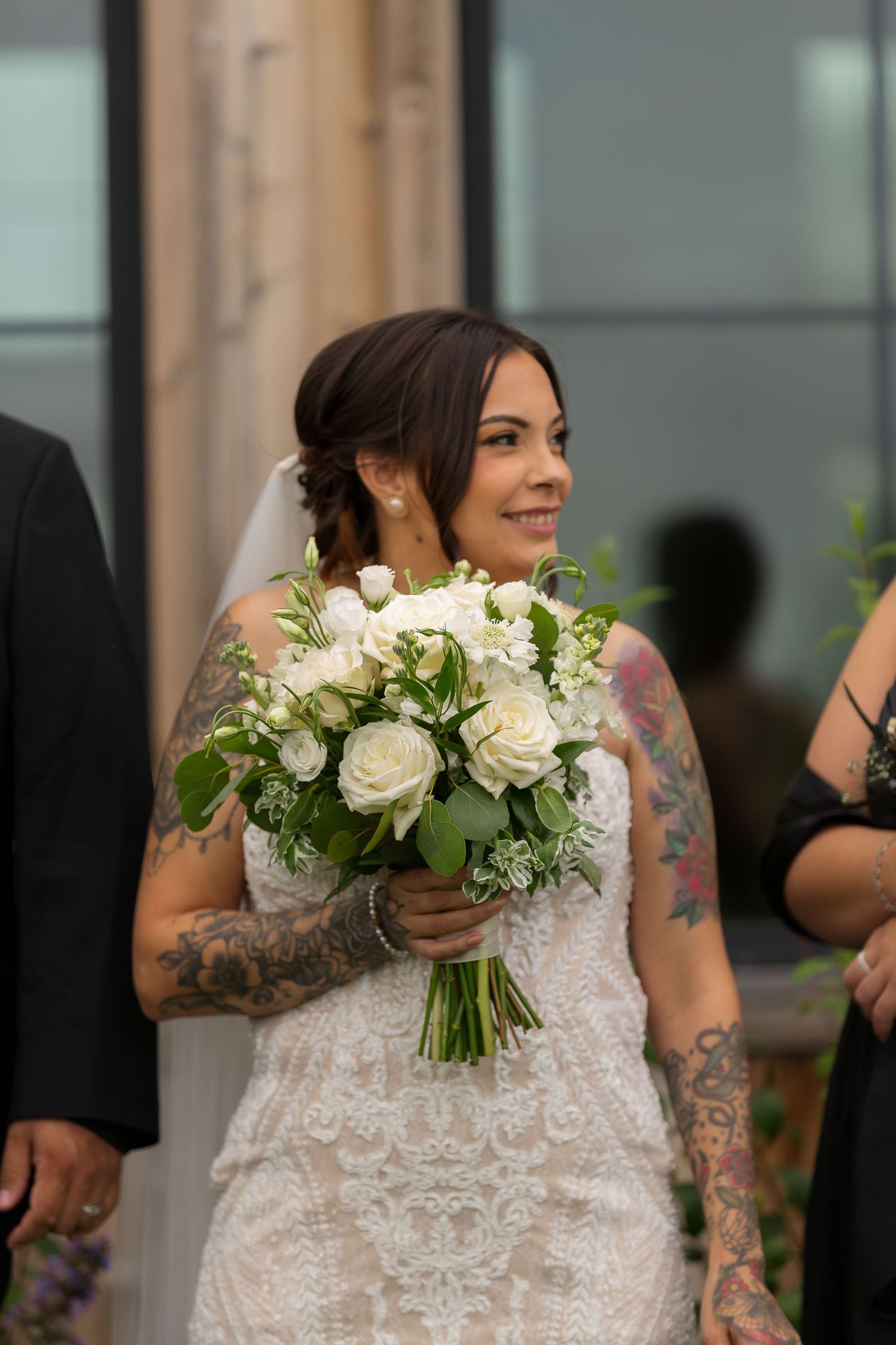 A bridal bouquet of white roses and greenery held against a lace wedding dress at Barn at Wind's Edge in Saskatoon, Saskatchewan.