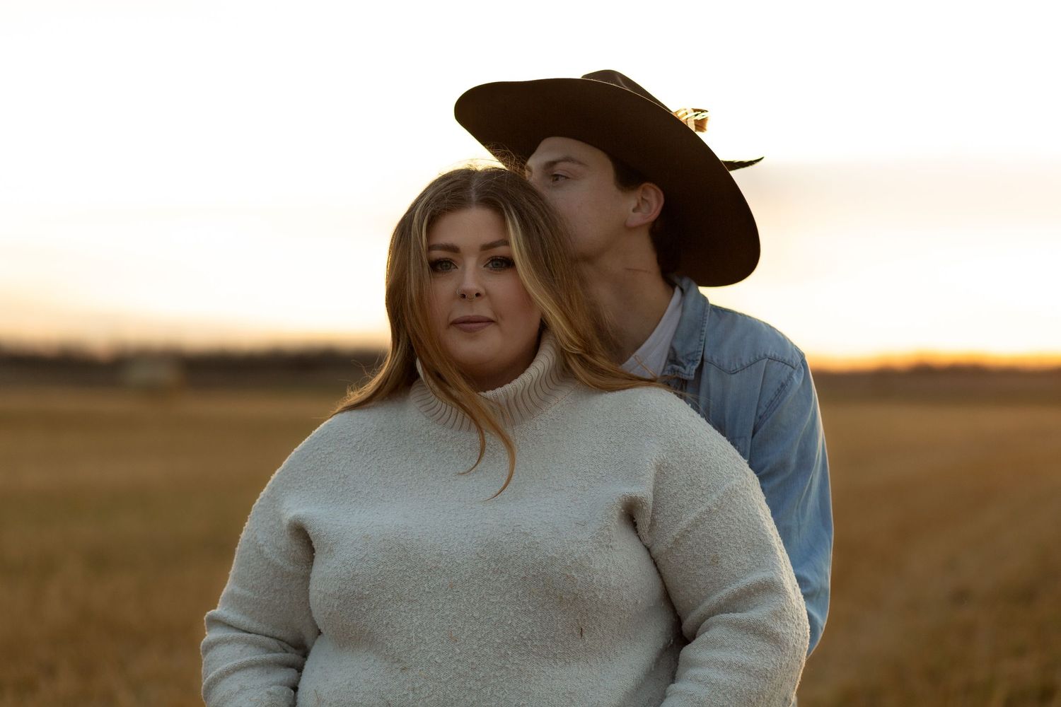 Couple in casual attire sharing an intimate moment at golden hour in a field in the Canadian Prairies.