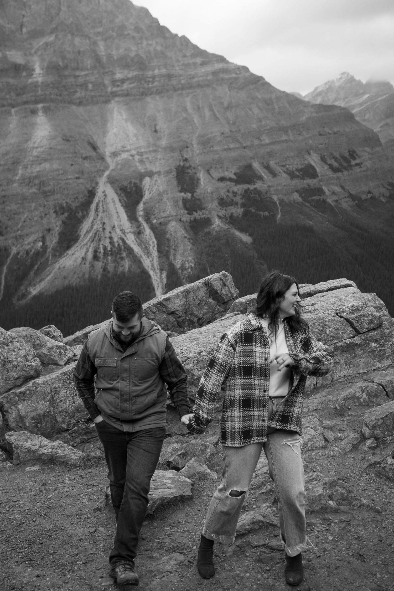 Couple holding hands while hiking on rocky mountain trail in black and white photography.