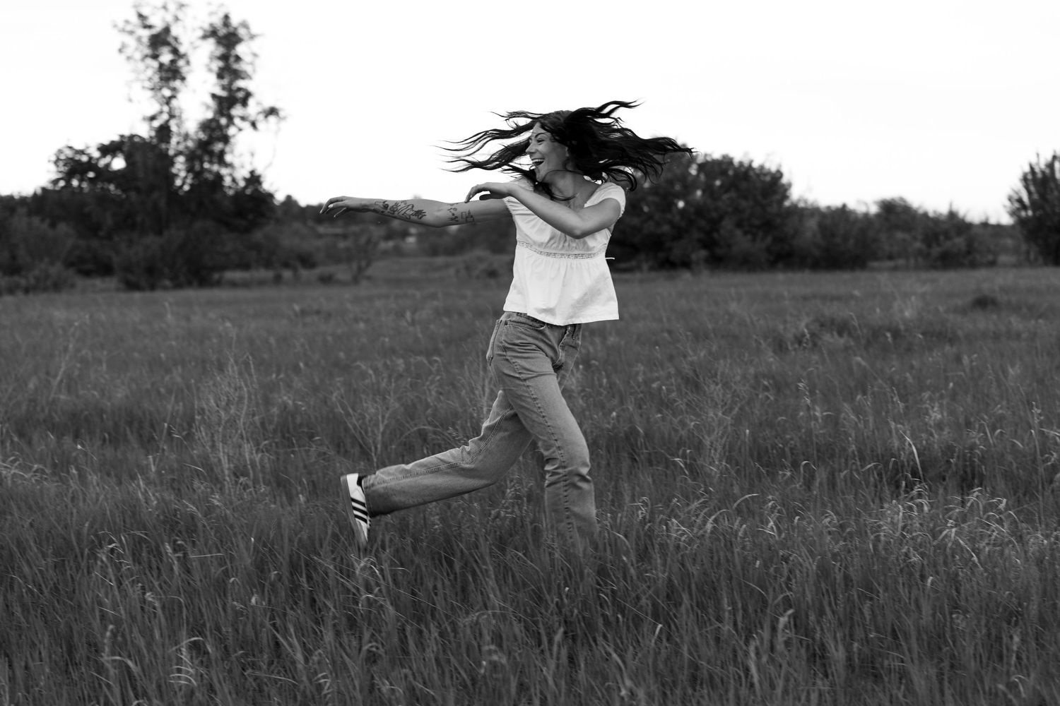Black and white photo of a woman running joyfully through a grassy field, her long hair flowing in the wind.