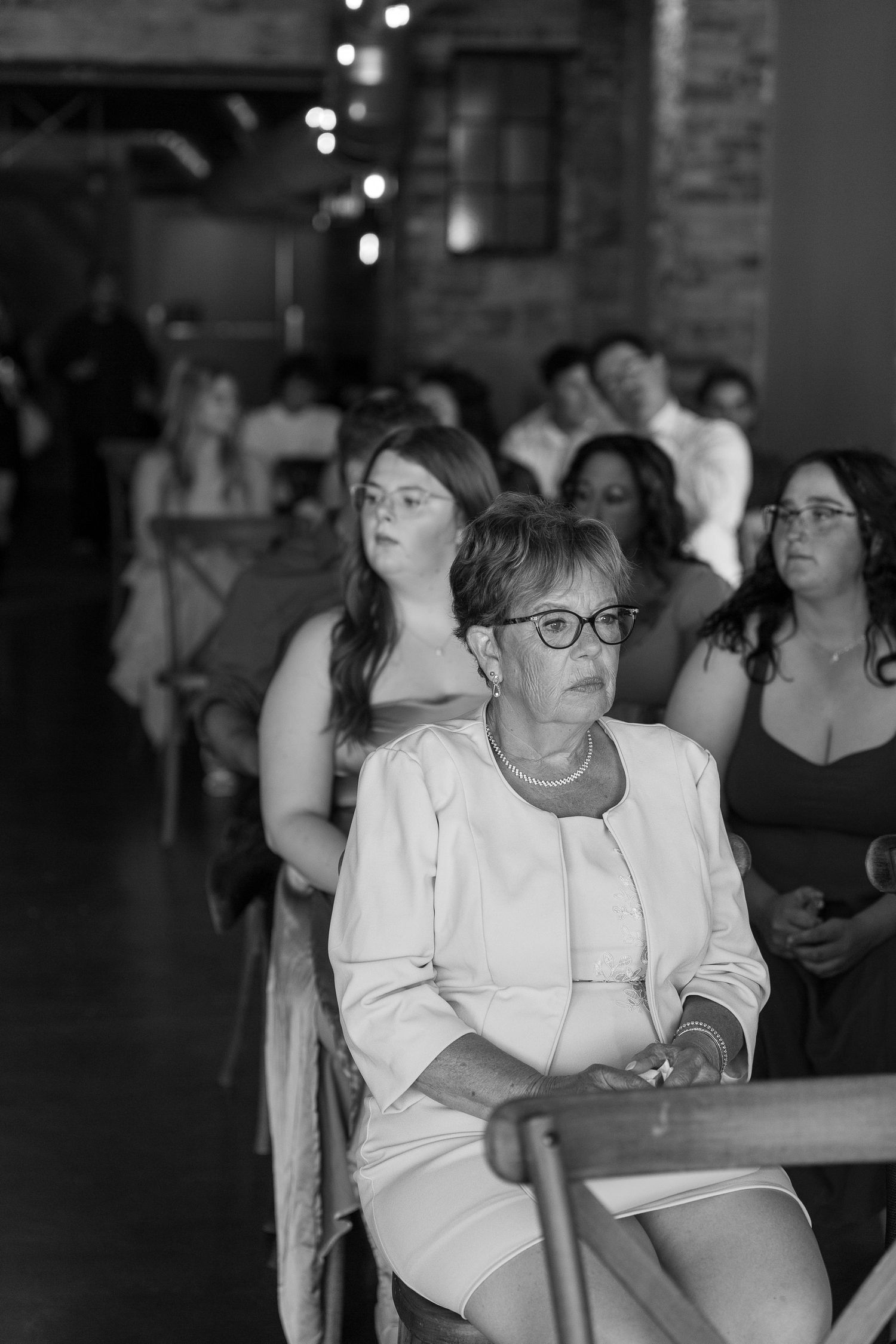 Black and white photo of wedding guests seated in pews during an indoor ceremony.