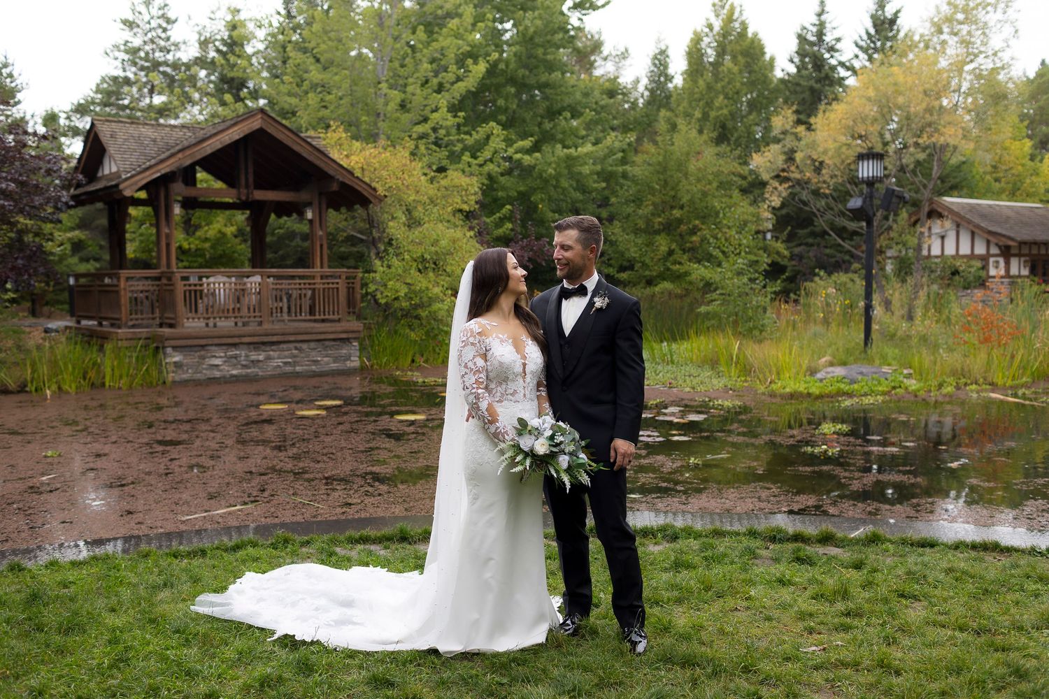 Wedding couple poses in front of rustic wooden gazebo on rainy day at Boffin Gardens.