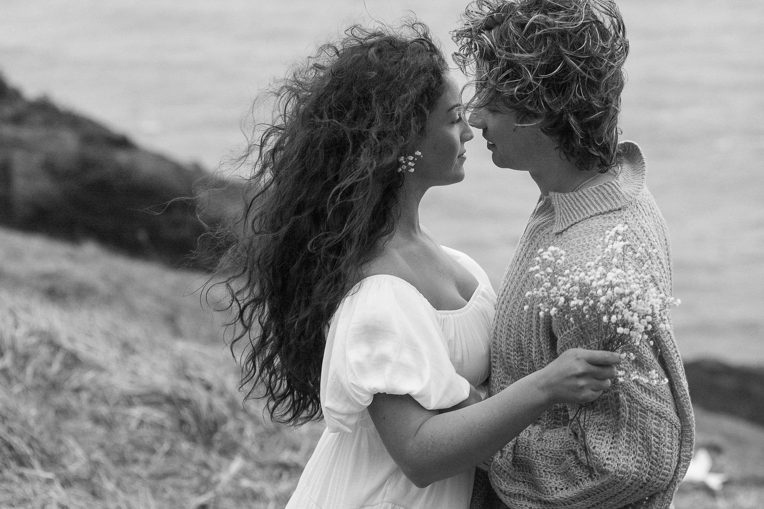 Intimate moment between couple on coastal hillside in black and white.