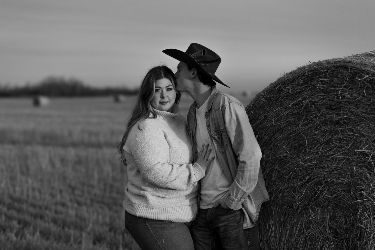A couple shares an intimate moment against a rustic outdoor backdrop at sunset.