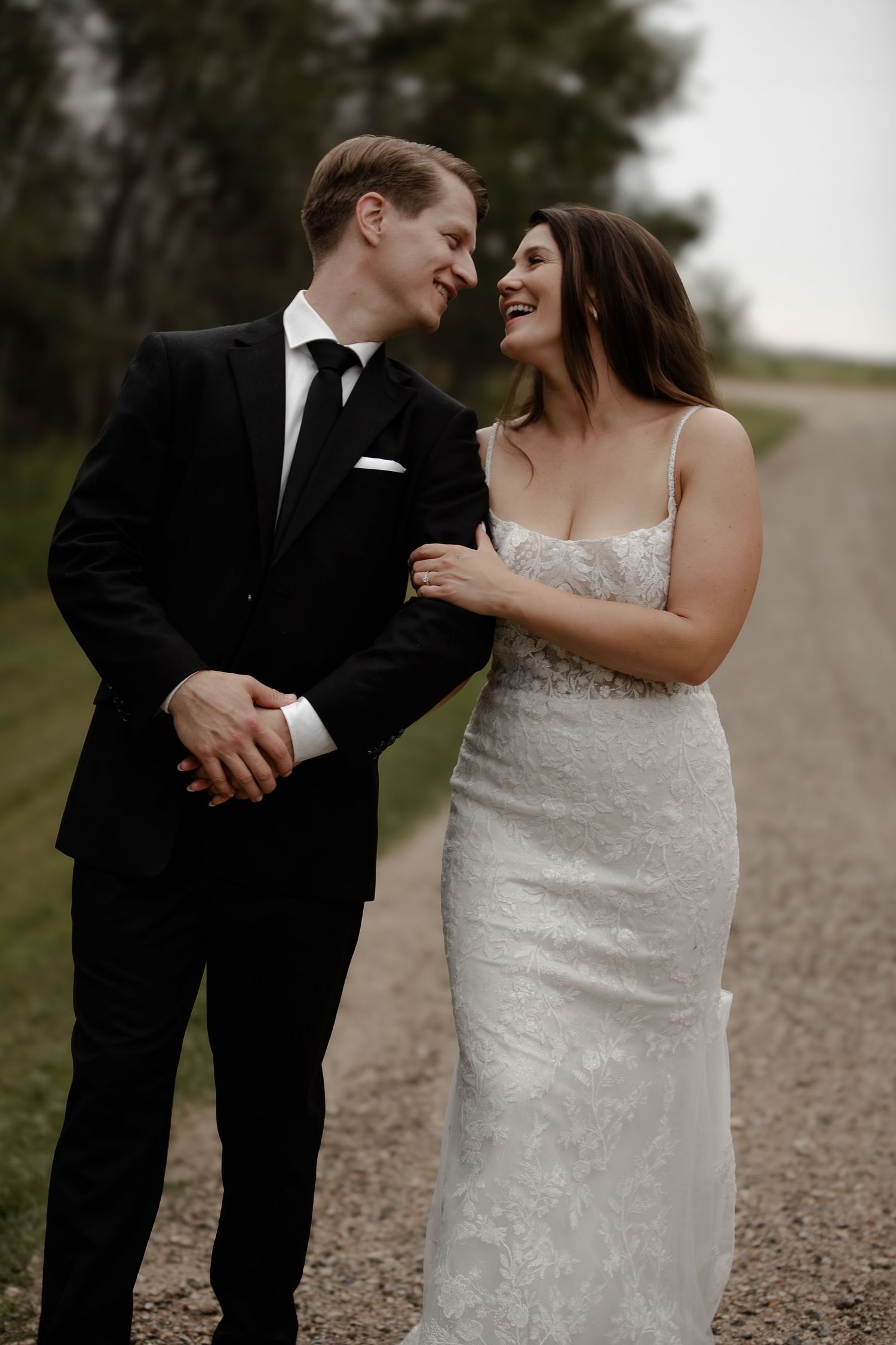 Couple shares intimate moment on dirt road during wedding photoshoot.