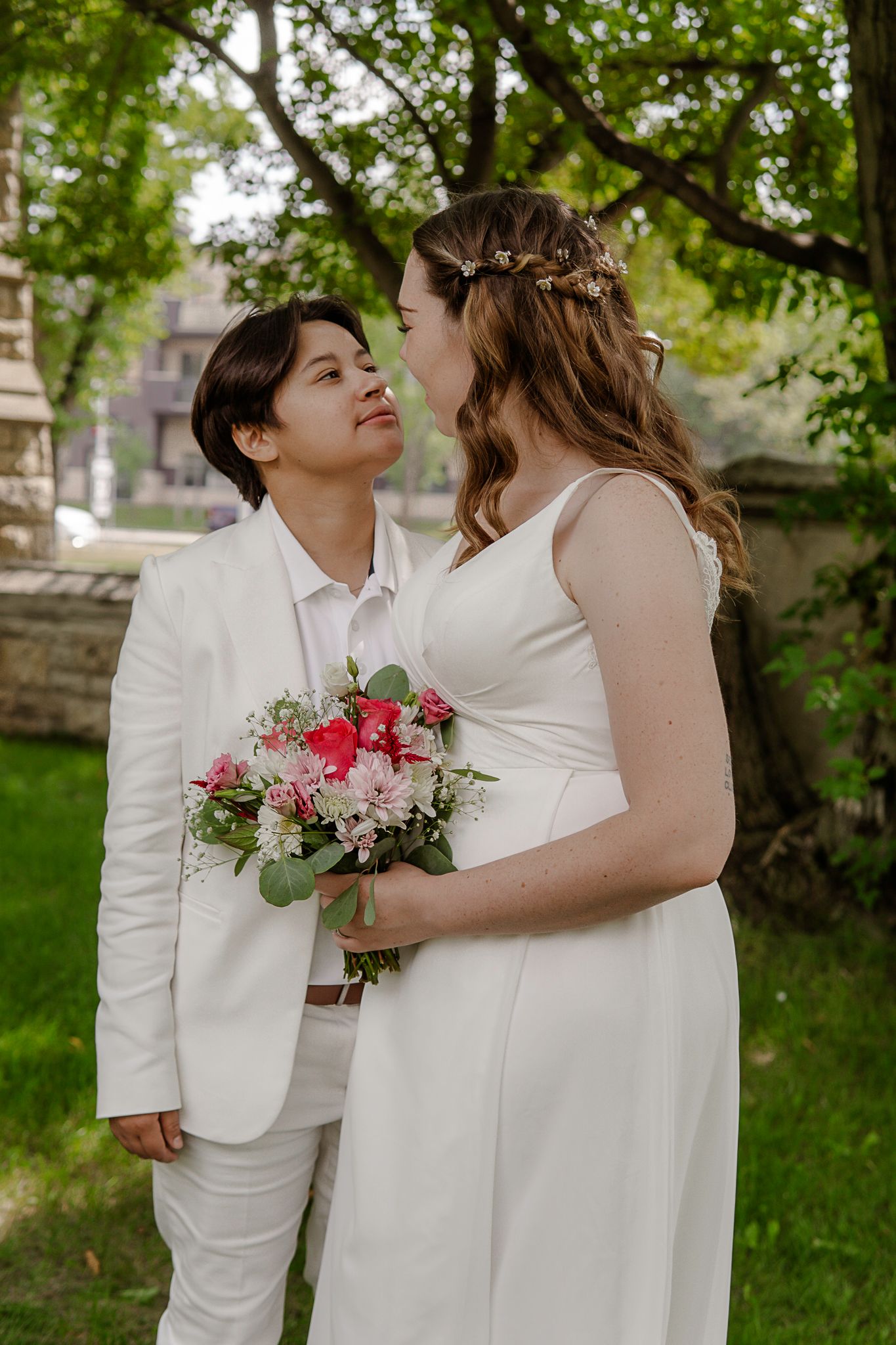 A couple in white outfits shares an intimate moment in a garden setting.