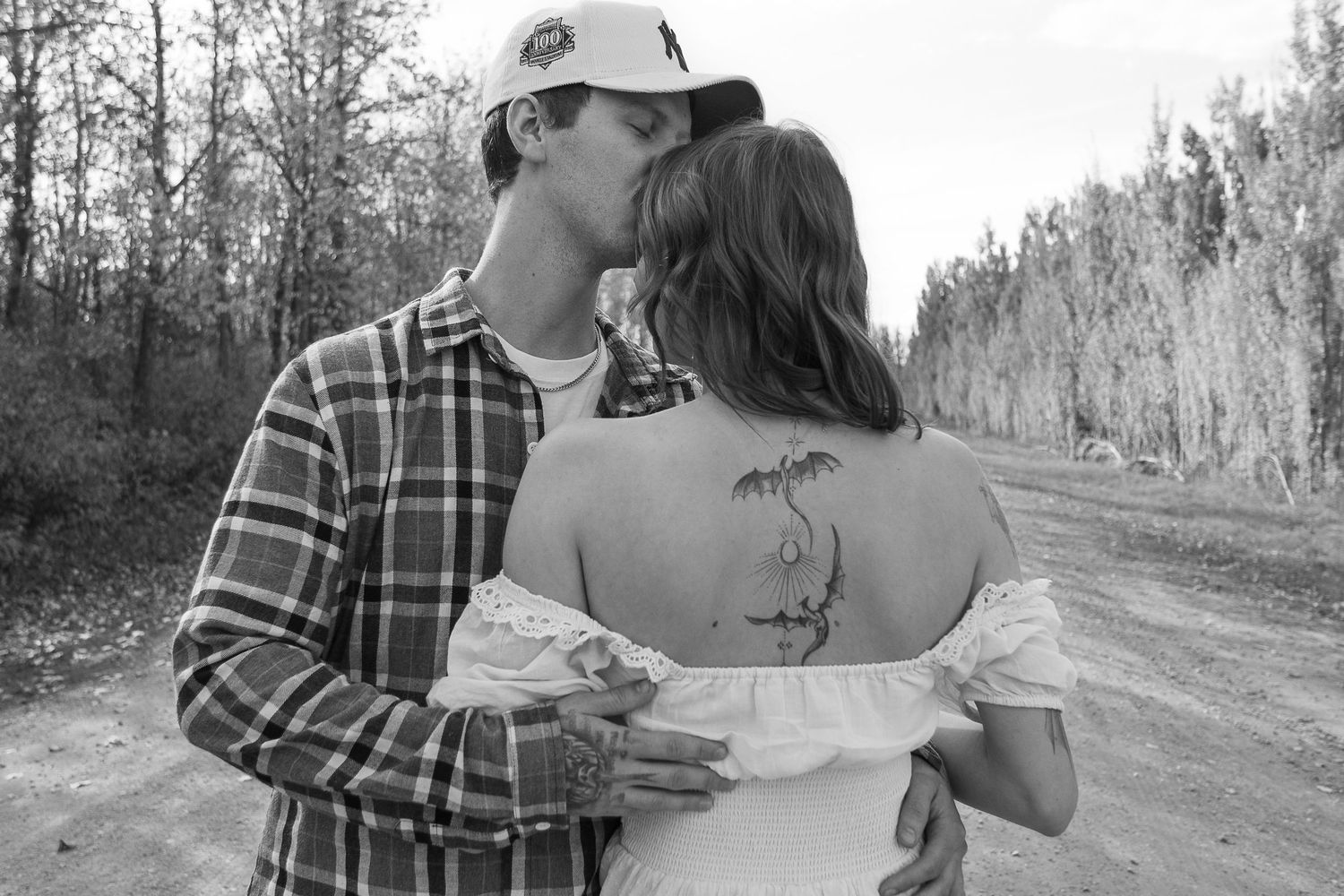 A black and white photo of a couple sharing a tender moment on a dirt road.