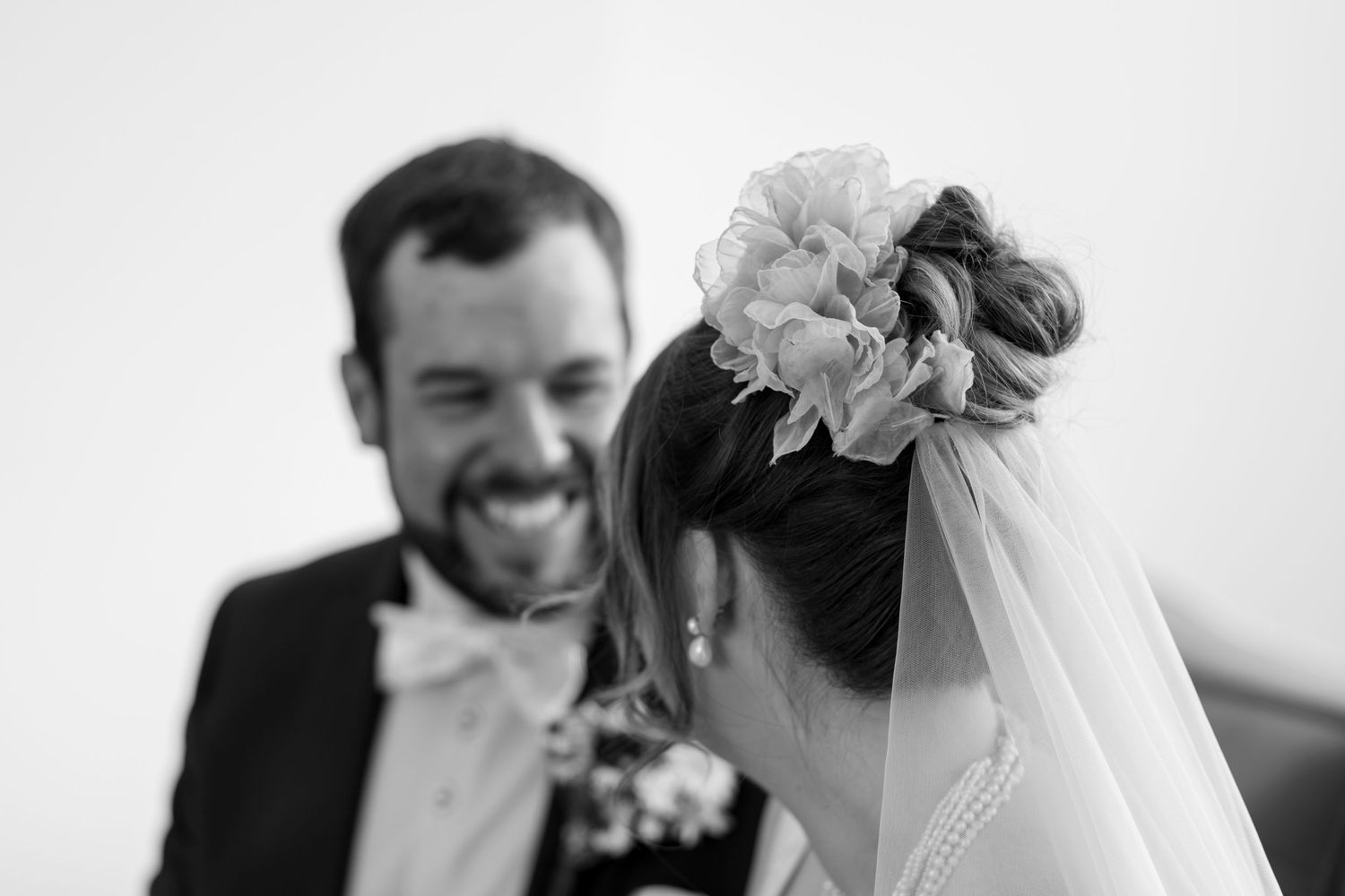 Black and white wedding photo of smiling groom and bride with floral hair accessory and veil.