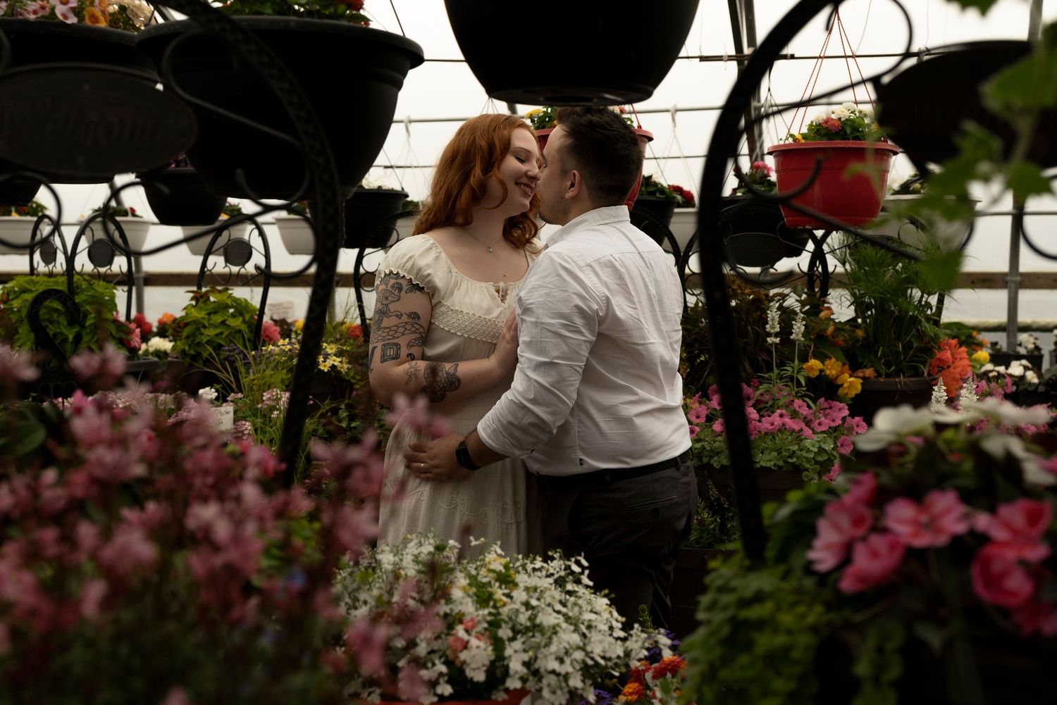 Couple sharing a romantic kiss surrounded by colorful blooming flowers inside a lush greenhouse wedding setting.