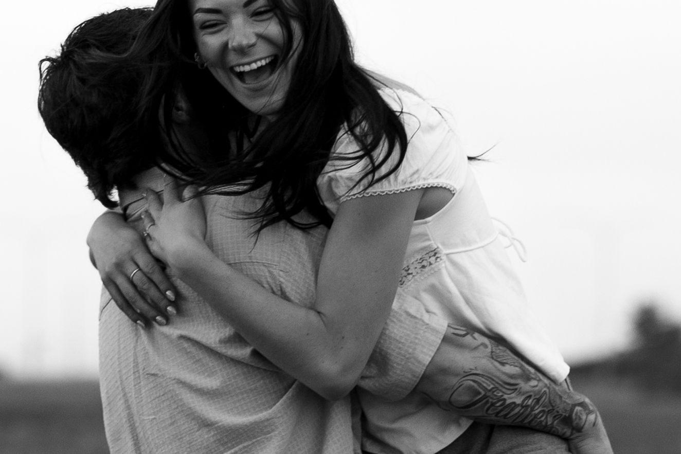 Black and white photo of two women joyfully embracing, one laughing and lifting the other outdoors.