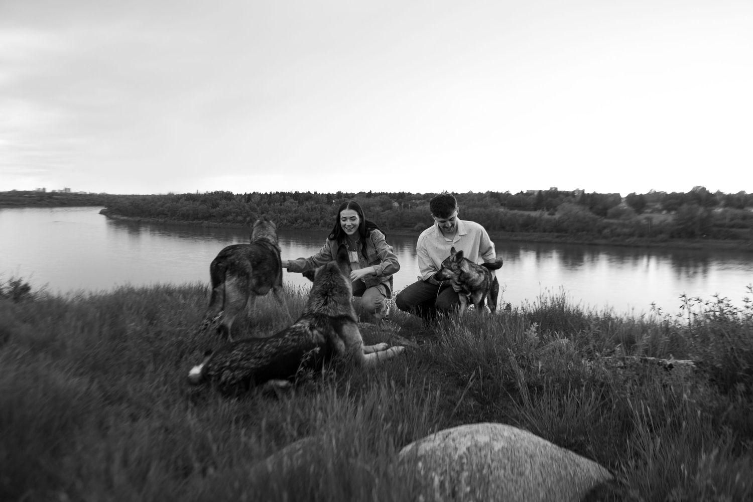Black and white photo of a group of friends relaxing by a river in a grassy field at dusk.