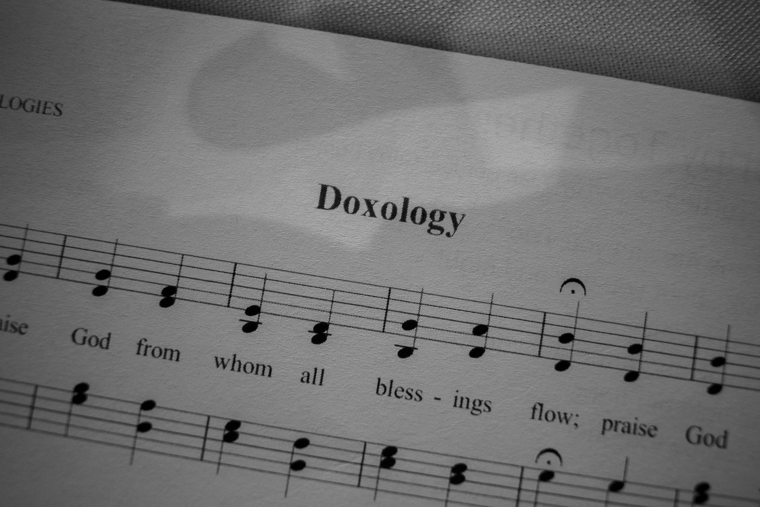 Black and white sheet music for the Doxology hymn, showing musical notes and lyrics beginning with 