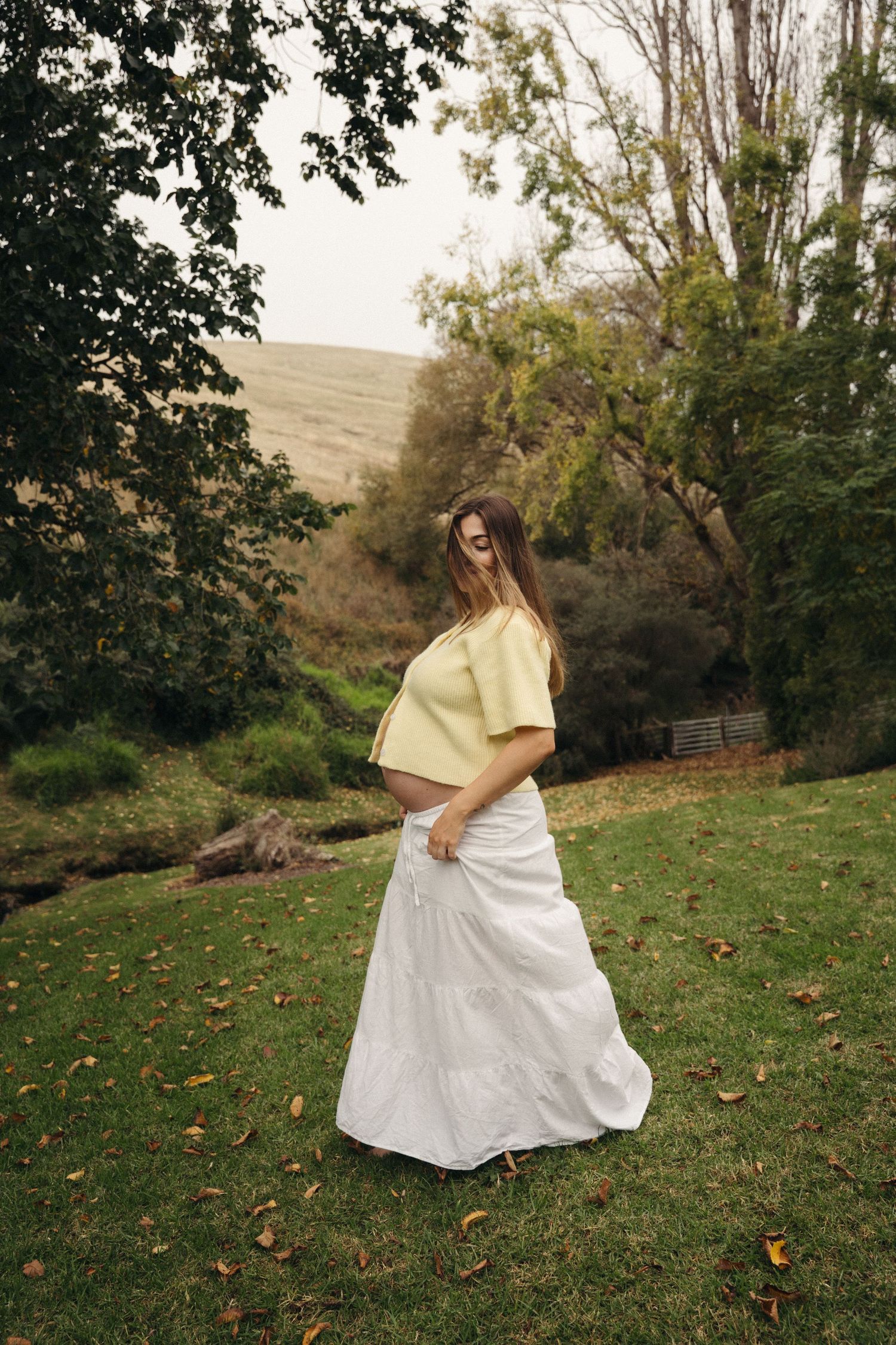 A pregnant woman dancing in a field at the end of her pregnancy in the hills at sunset at a maternity family photography session.