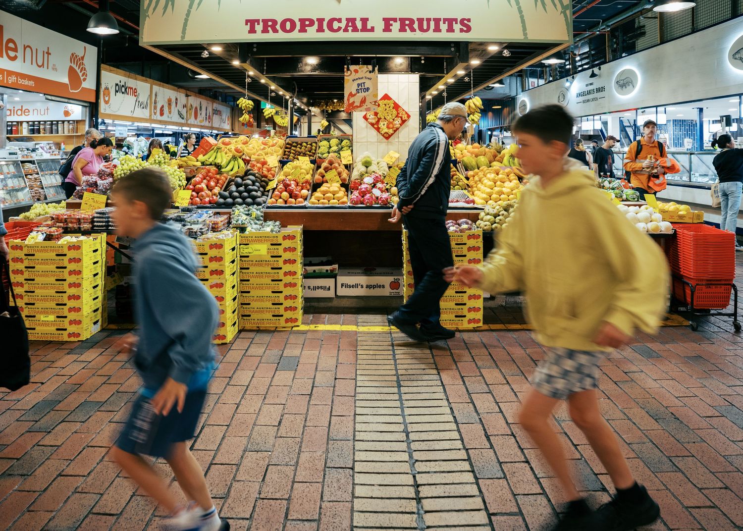 Boys running through the colourful Central Markets in Adelaide on a day trip with their family during a family photo shoot.