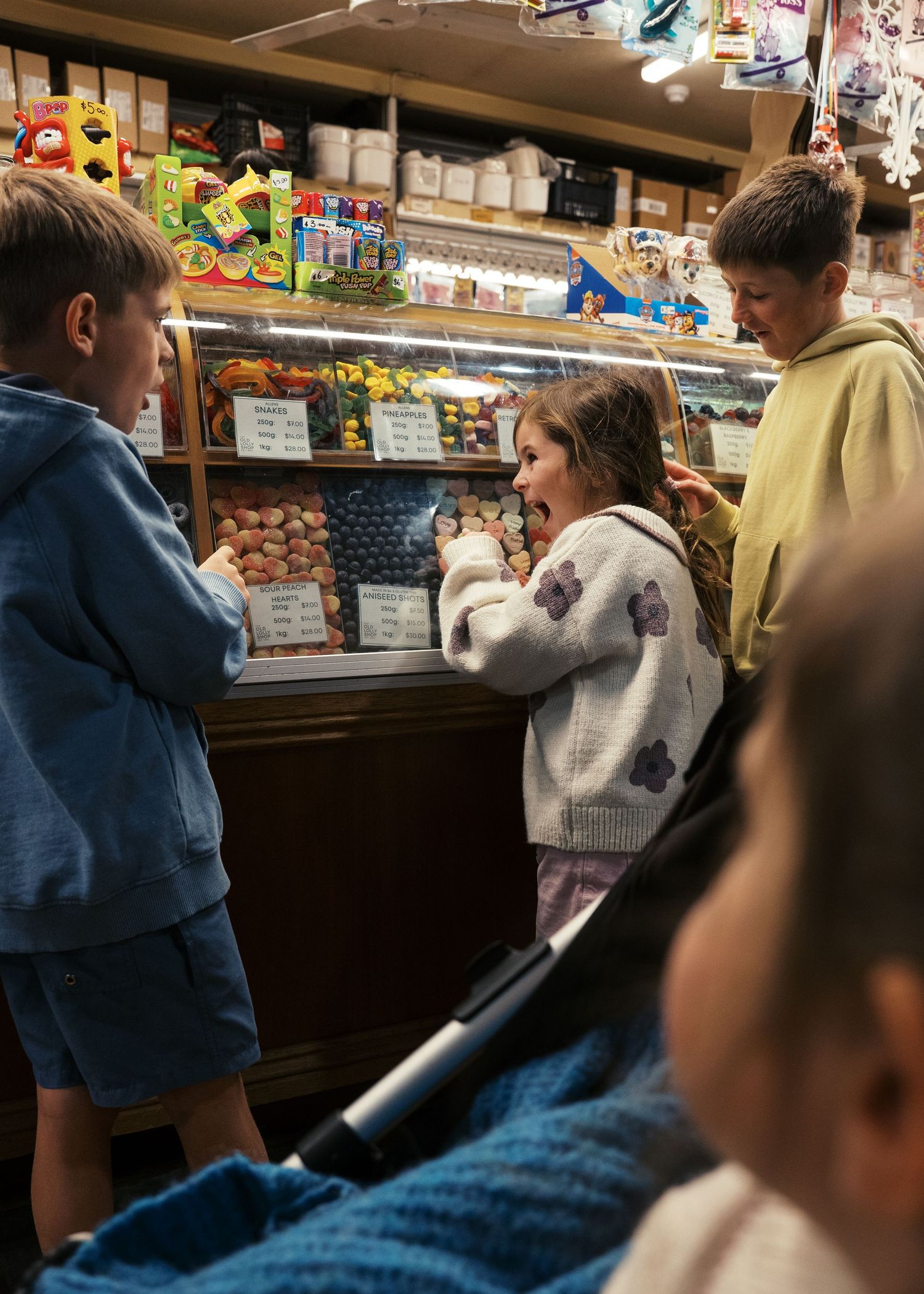 Siblings at a lolly store choosing their favourite lollies with their mum and grandma during a family photoshoot.