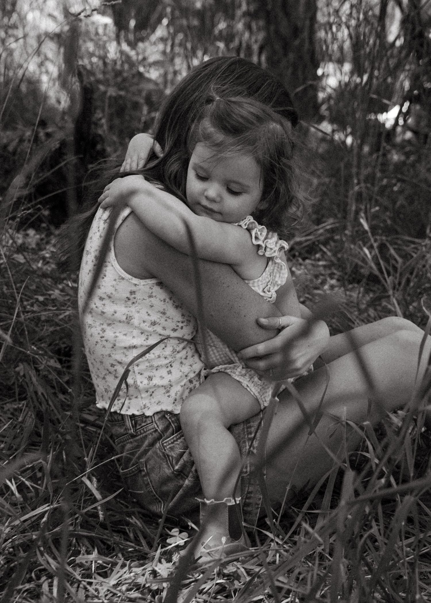 A mother and daughter cuddling in the forest at a motherhood photography session.