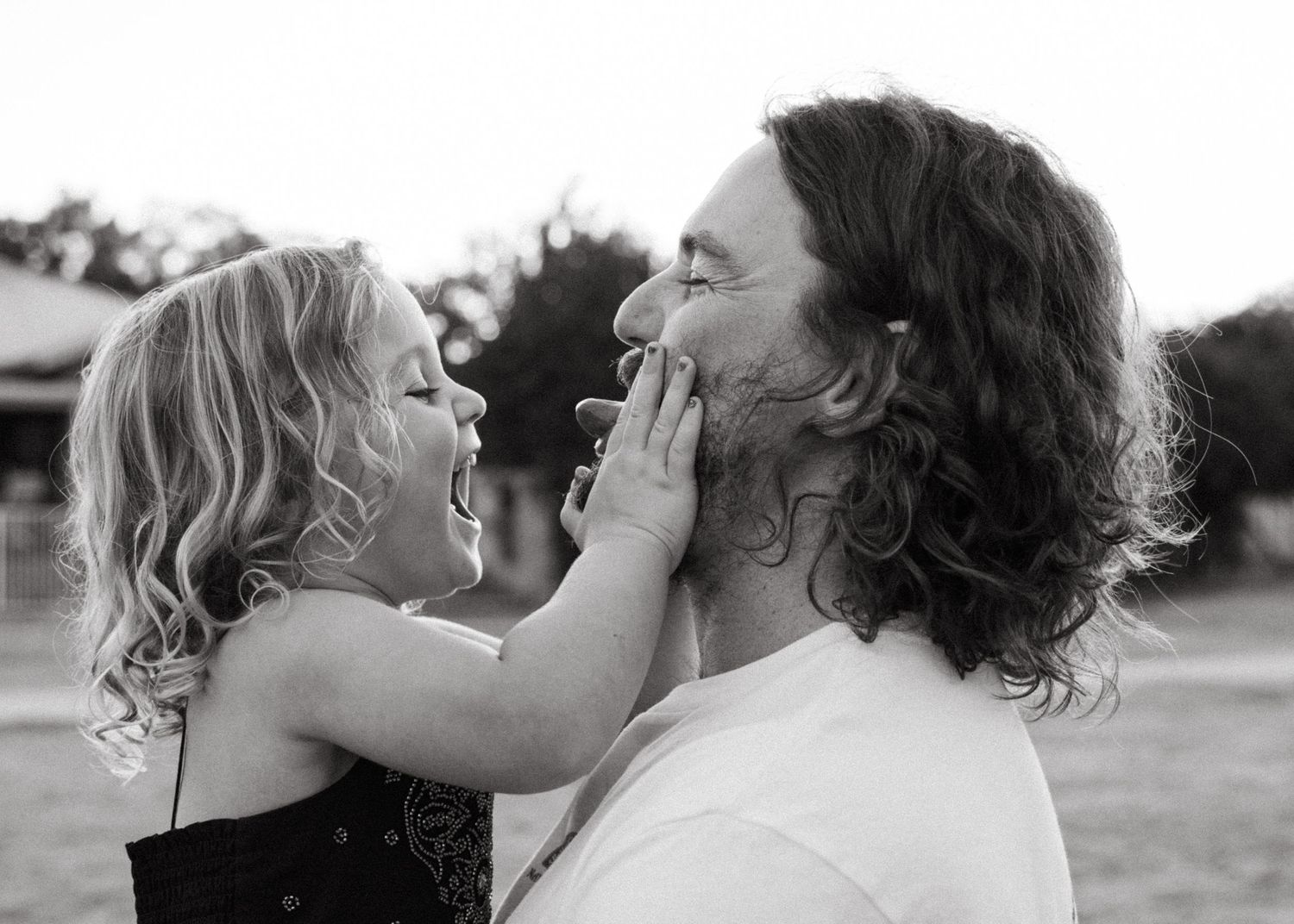 A father and his toddler daughter cuddling and laughing at a family photoshoot at sunset.