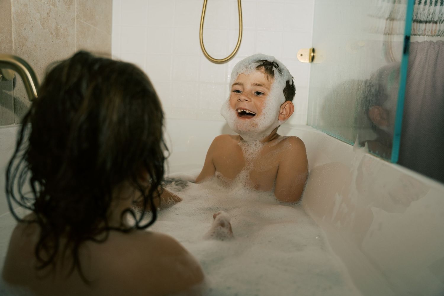 Kids in the bath with bubbles on their face like Santa Claus laughing and having fun at a family photoshoot at home.