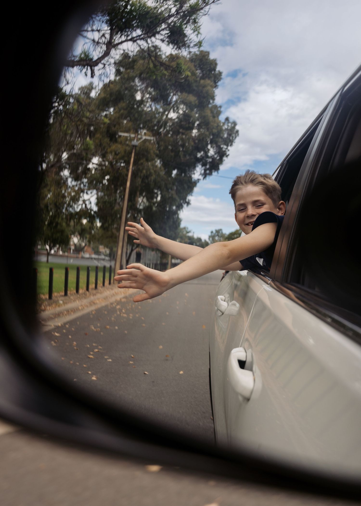A boy hanging out the window of a car feeling the wind in his face, arms stretched out, experiencing the world during a family photoshoot.