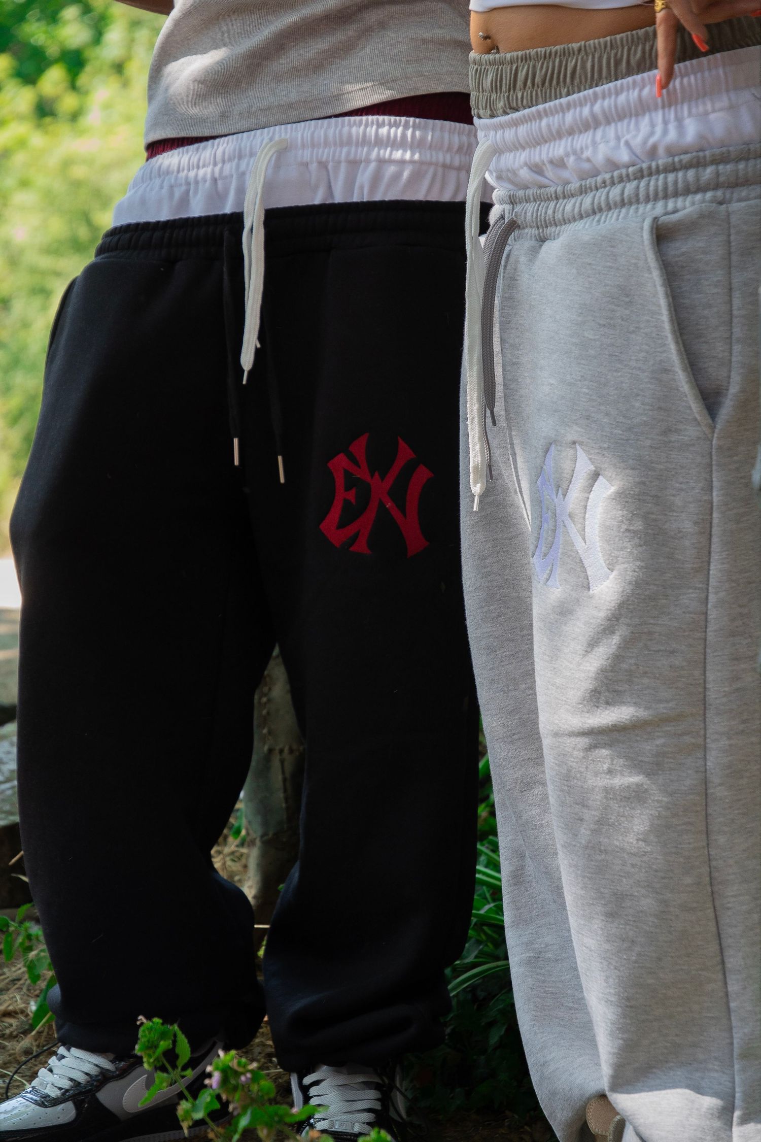 Two people wearing NY Yankees logo sweatpants in black and gray colorways, standing outdoors.