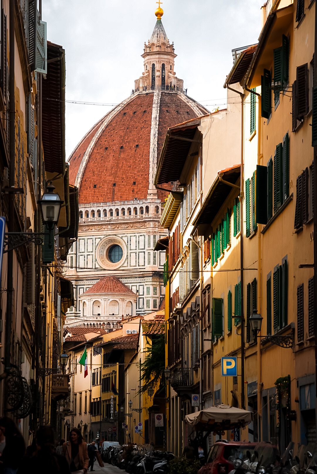 Narrow Florence street leading to the iconic Duomo cathedral dome, framed by colorful Italian Renaissance buildings in Tuscany.