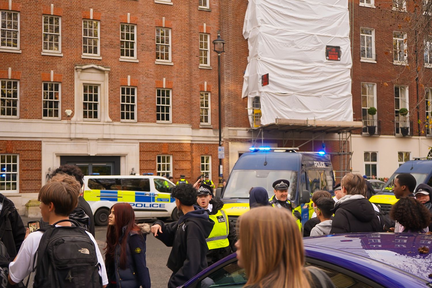 London police officers managing a crowd on a busy street near a scaffolded building.