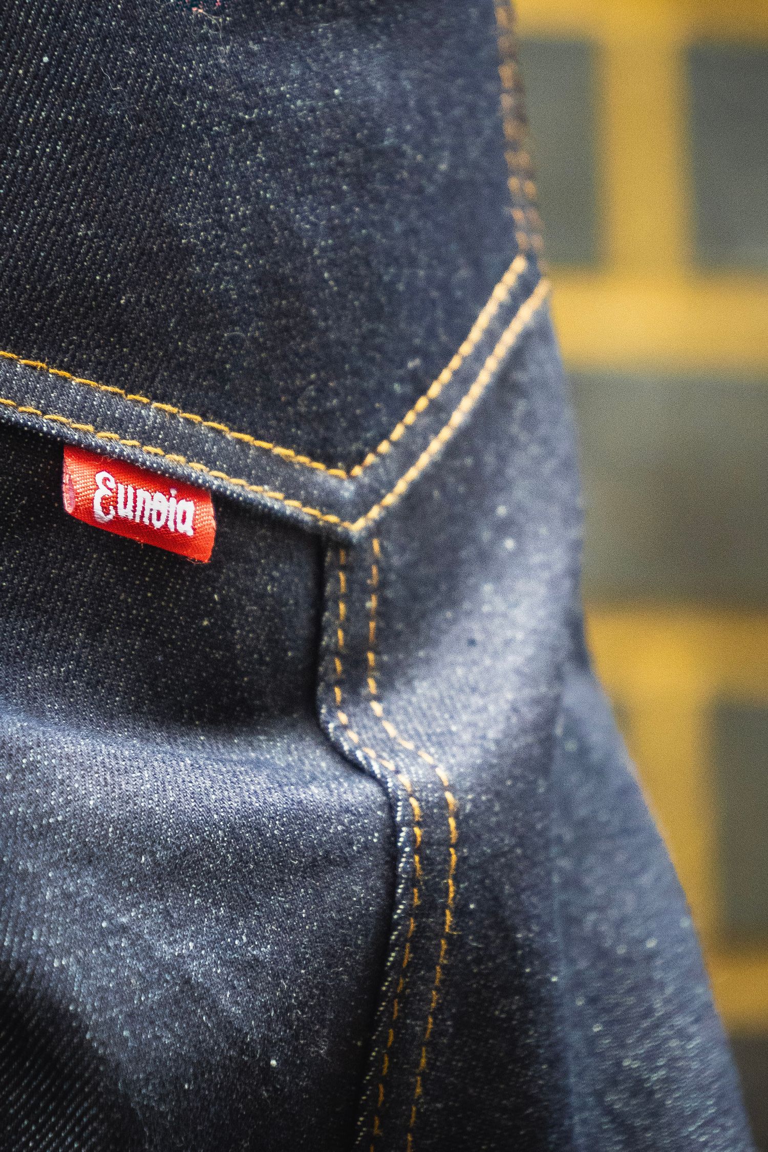 Close-up of dark denim jeans featuring a red Sundia brand label and gold contrast stitching on the back pocket.