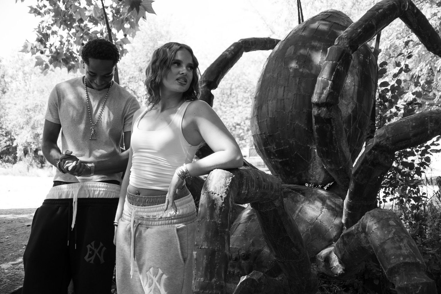 Black and white photo of two young people standing near a large sculptural art installation outdoors.
