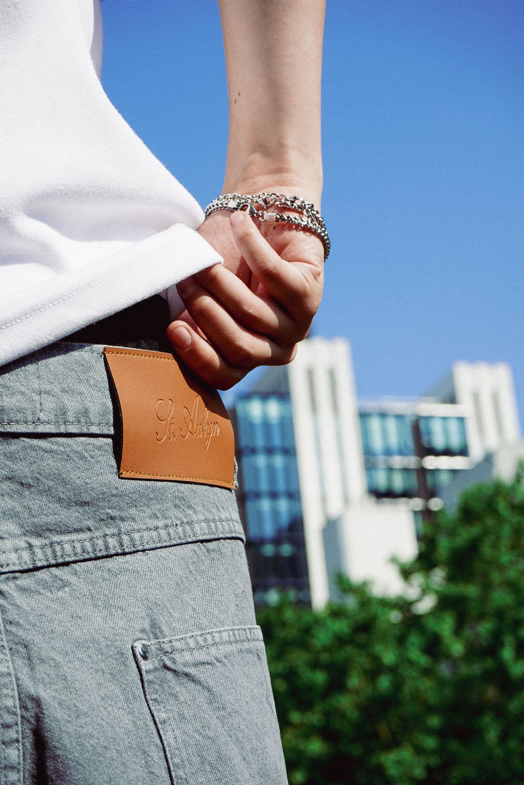 Close-up of a hand tucking a tan leather wallet into light blue jeans under a clear blue sky.