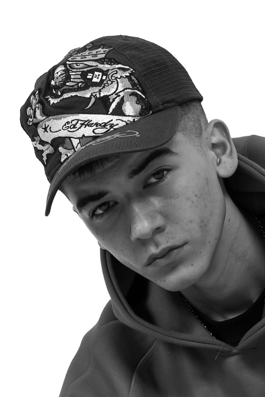 Close-up black and white portrait of young man wearing Ed Hardy graphic trucker cap and hoodie.