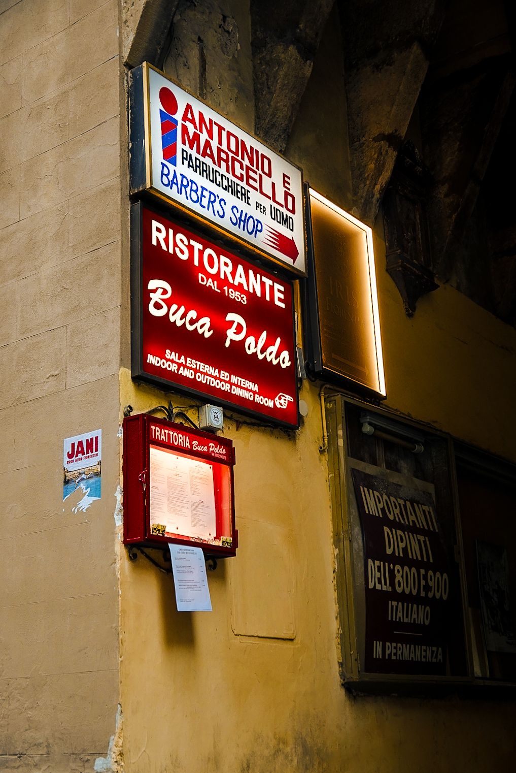 Italian restaurant Buca Poldo signs and barber shop signage on a rustic building wall in Italy.