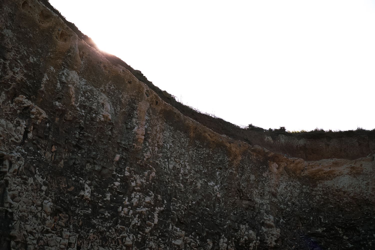 Sun peeking over a rugged rocky hillside with lichen-covered stones against a bright sky.