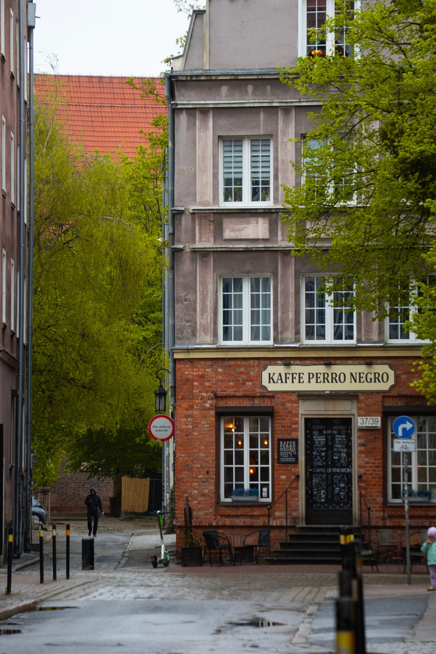 Kaffe Perro Negro cafe on a cobblestone street corner in Gdansk, Poland, featuring red brick architecture.