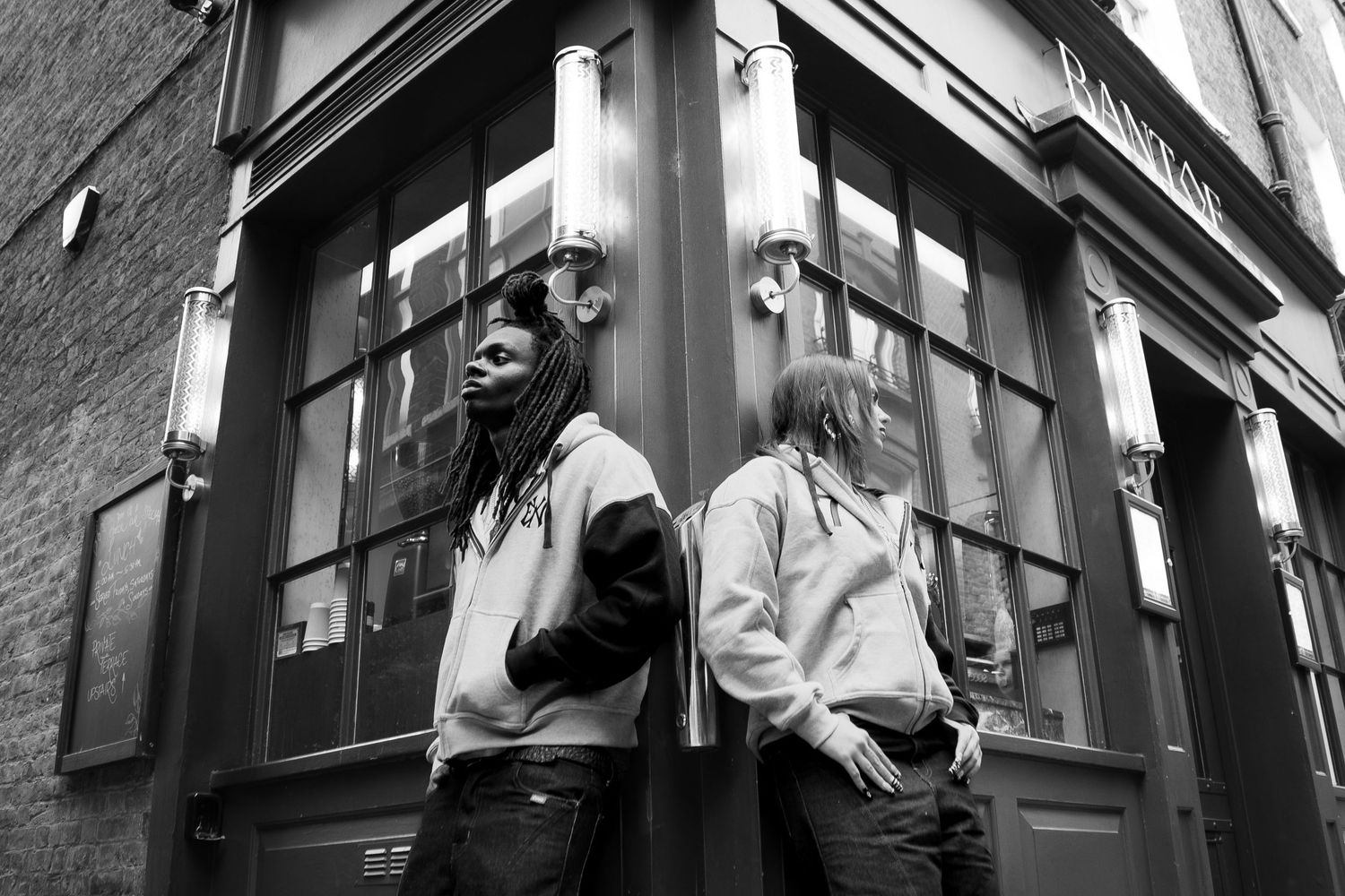 Two people standing back to back outside a vintage pub in a black and white street photography shot.