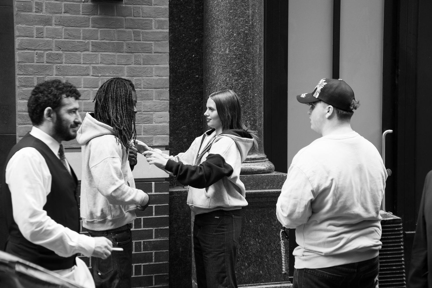 Black and white photo of four people conversing outside a brick building on a city street.