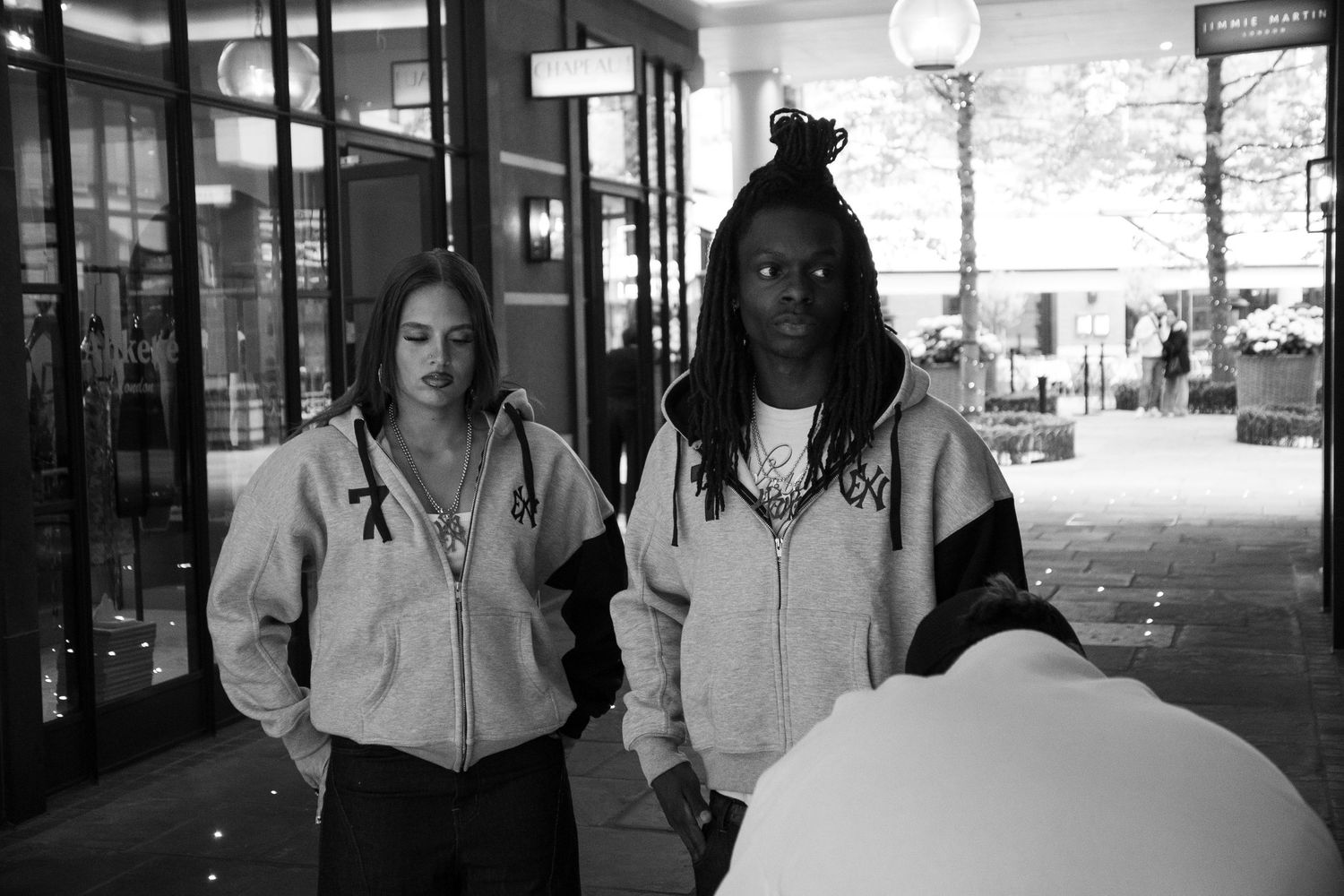 Two women in matching hoodies pose outside a building in a black and white street photo.