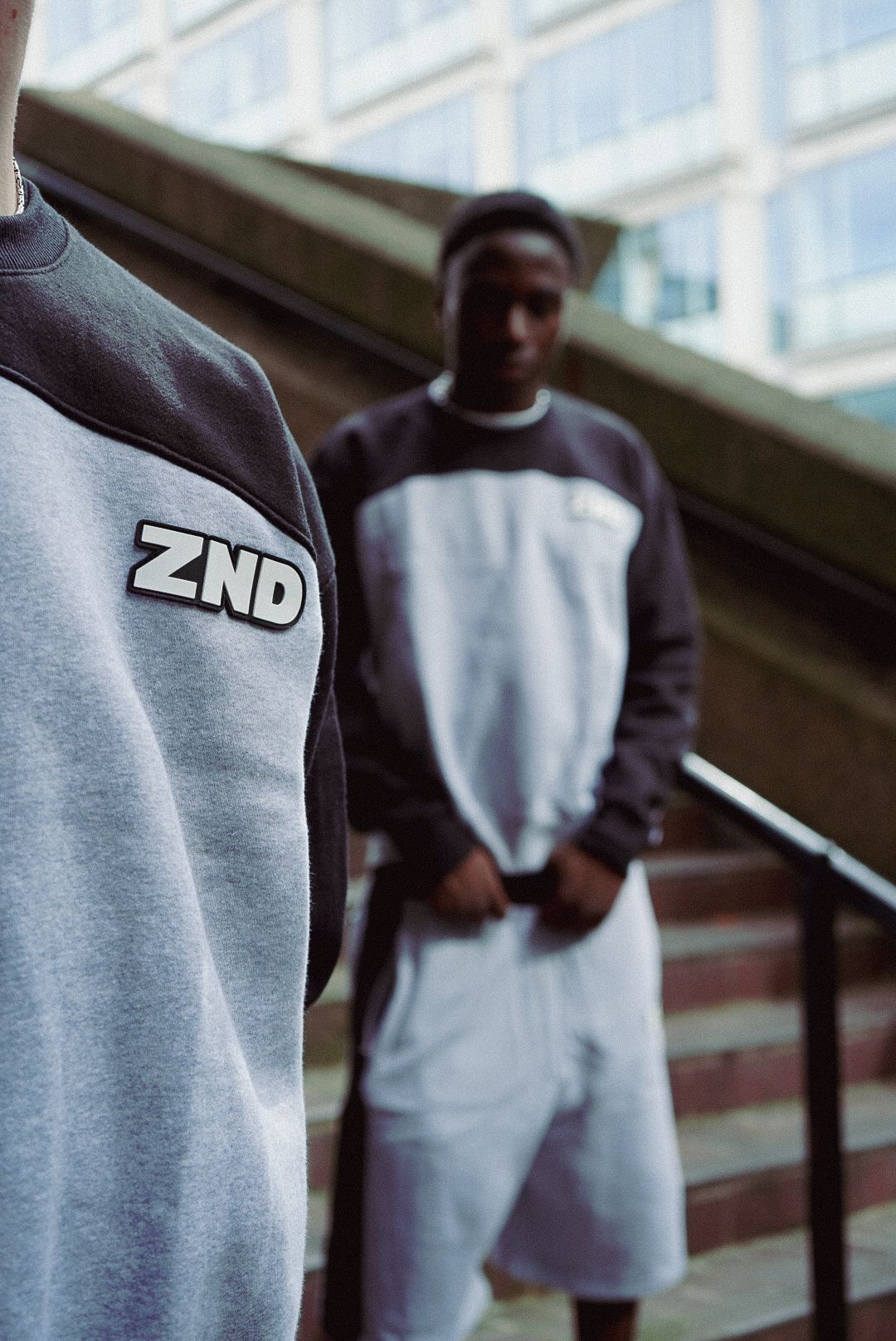 Two men wearing ZND branded grey and dark sweatshirts posing on urban staircase.