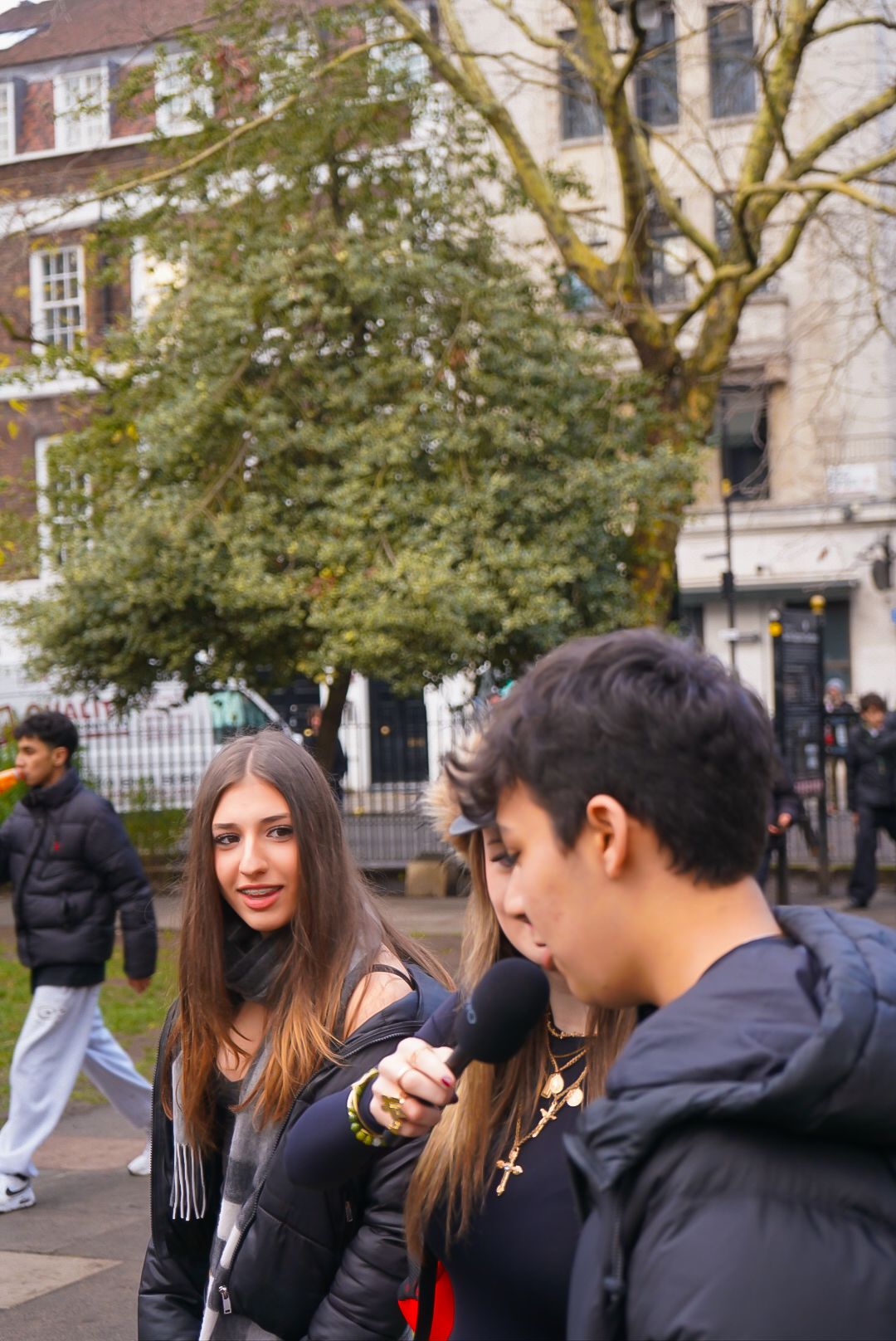 Two young people in black outfits, one holding a microphone, in a London park setting.