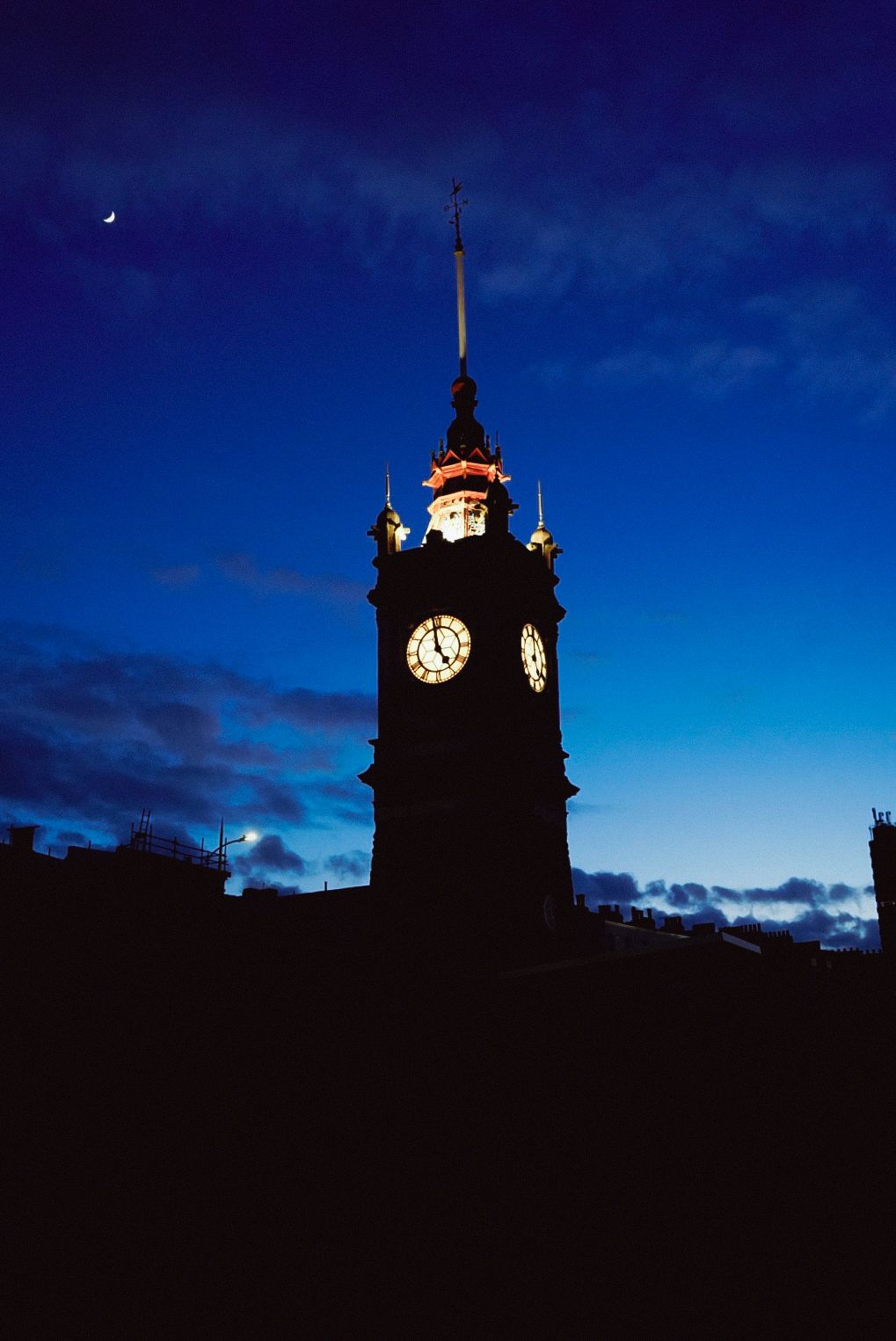 Silhouette of a historic clock tower against a deep blue twilight sky with crescent moon.