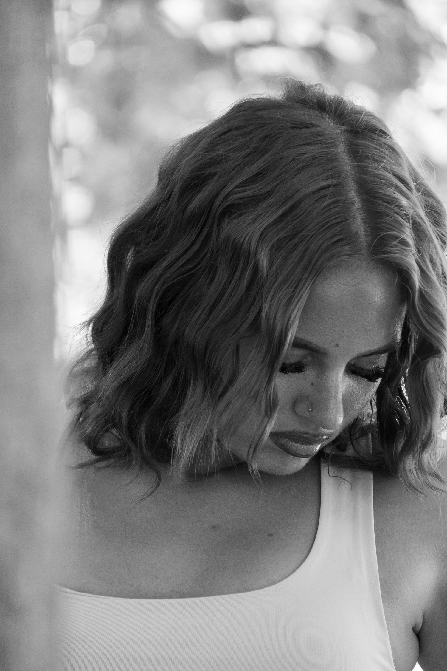 Black and white portrait of a young woman with wavy bob hair looking down, outdoors.