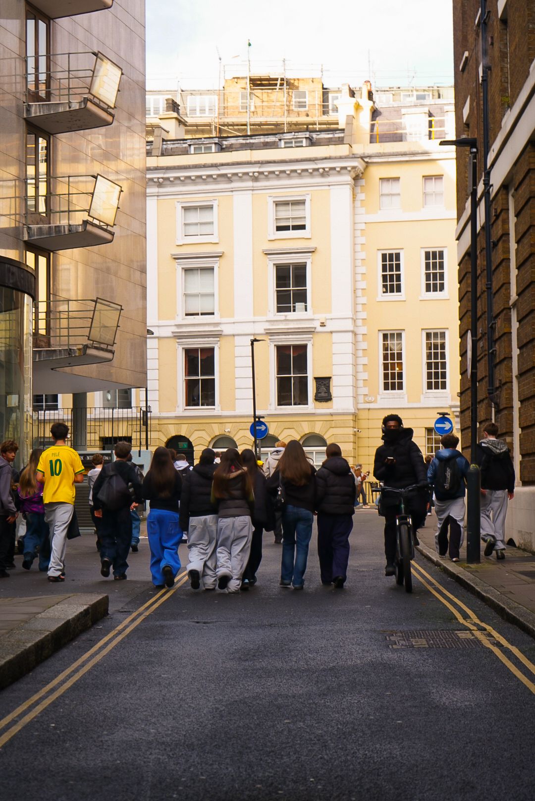 Group of young people walking down a narrow London street toward a yellow Georgian building.