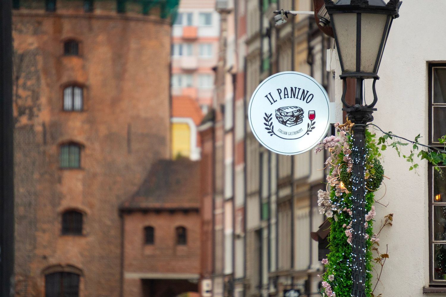 Il Panino restaurant sign on a historic European street with brick buildings and a vintage lamp post.