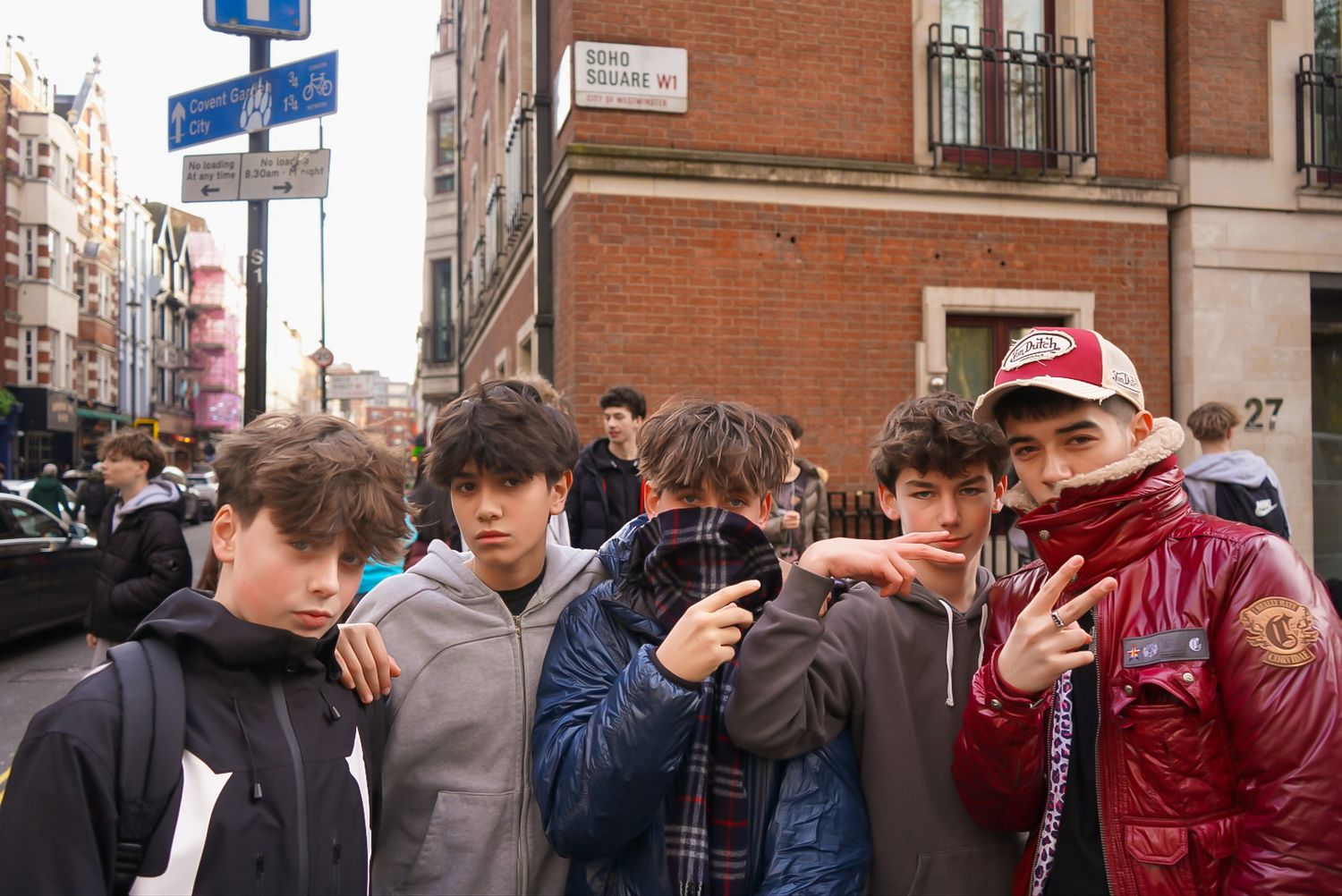 Group of teenage boys posing on a busy urban street with city buildings in the background.