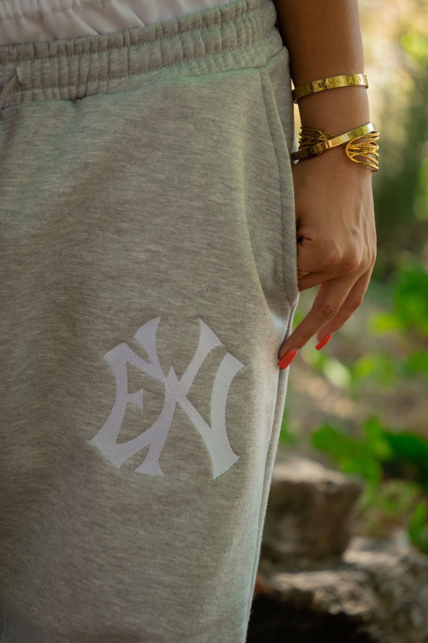 Gray sweatpants with NY logo design, worn by a woman with gold bracelets and red nails.