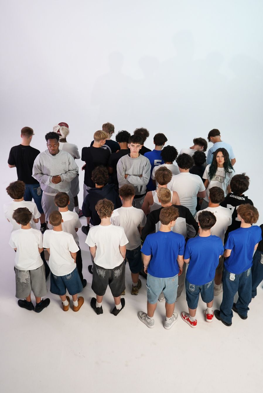 Large group of young people gathered in a circle viewed from above against a white background.