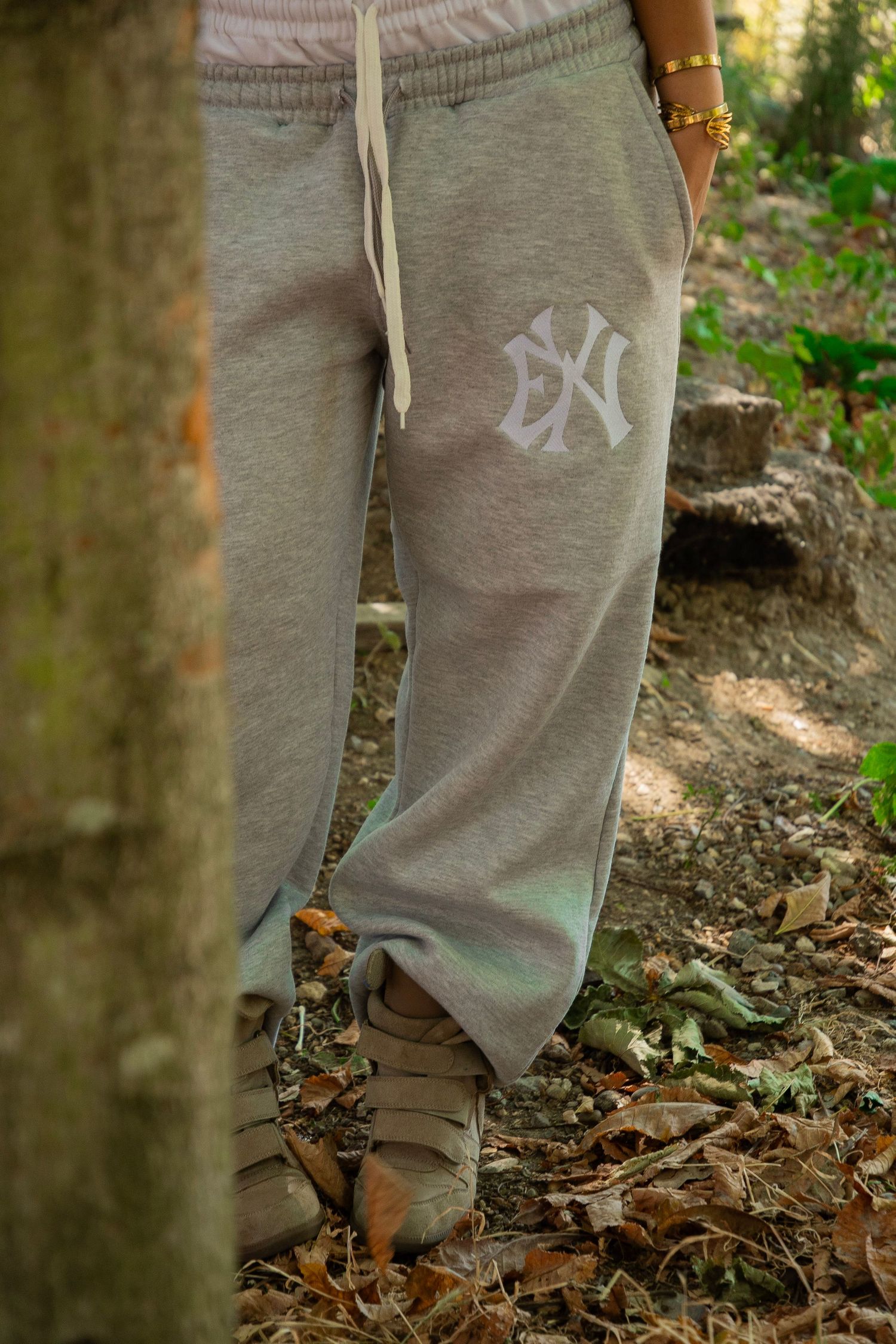 Gray NY Yankees sweatpants with embroidered logo, worn with tan sneakers in a wooded outdoor setting.