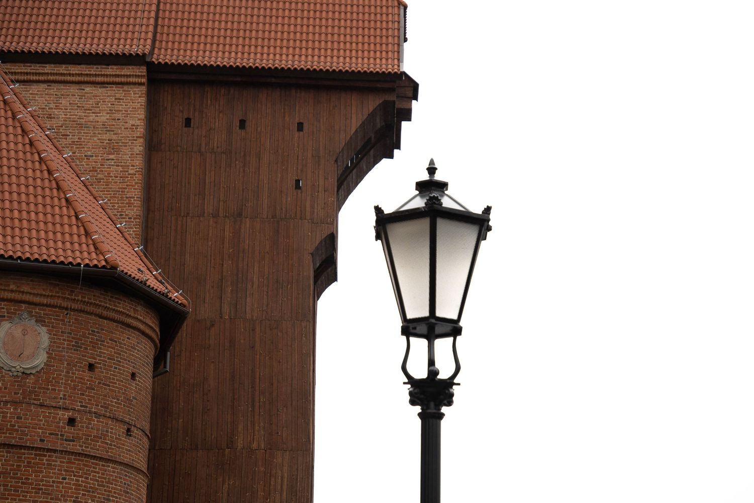 A classic black street lamp post stands in front of a historic red brick building with a terracotta tiled roof.